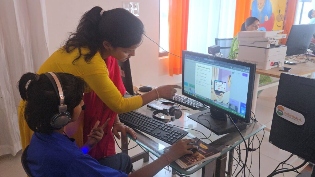 Teacher guiding a student while learning on a computer in an Apni Pathshala Learning POD, showing hands-on digital learning and personalized support.